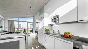 Une cuisine moderne avec des meubles blancs, un four à micro-ondes encastré et un évier en acier inoxydable.