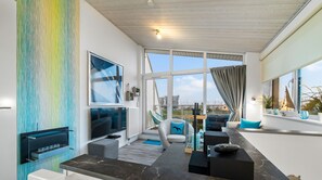 Ein modernes Wohnzimmer mit großem Fernseher, bequemen Sitzmöglichkeiten, Blick auf die Stadt und einer Segelboot-Dekoration.