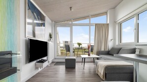 A modern living room with a flat-screen TV, a sofa, a coffee table, and a balcony with a view of the city. - Ferienhaus Sonnenblume Marina Wendtorf (Wendtorf)