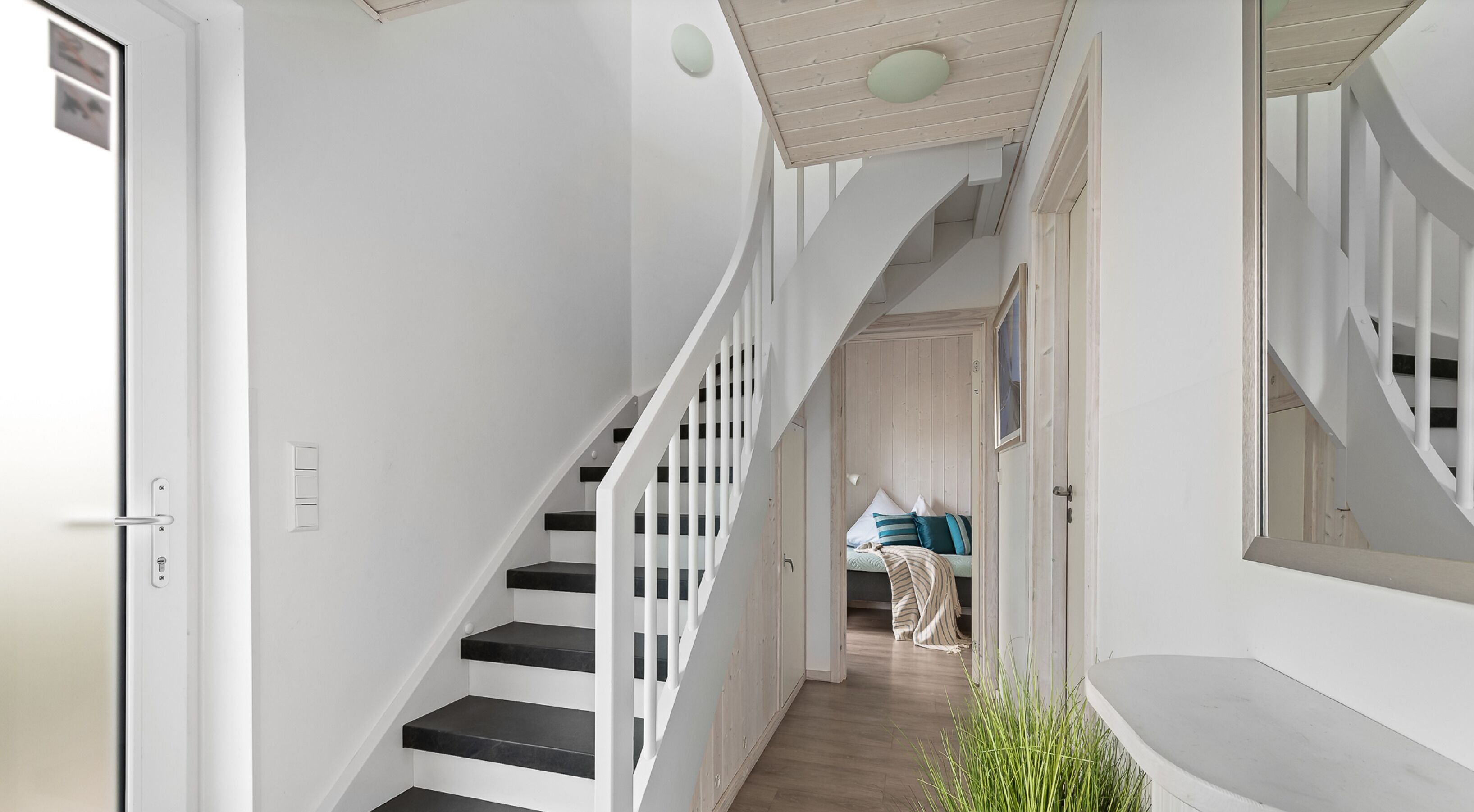 Un escalier avec des rampes blanches et des marches noires menant à une chambre à coucher où se trouvent un lit et une table de chevet.