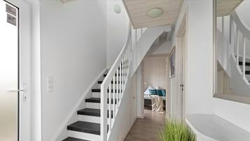 Un escalier avec des rampes blanches et des marches noires menant à une chambre à coucher où se trouvent un lit et une table de chevet.