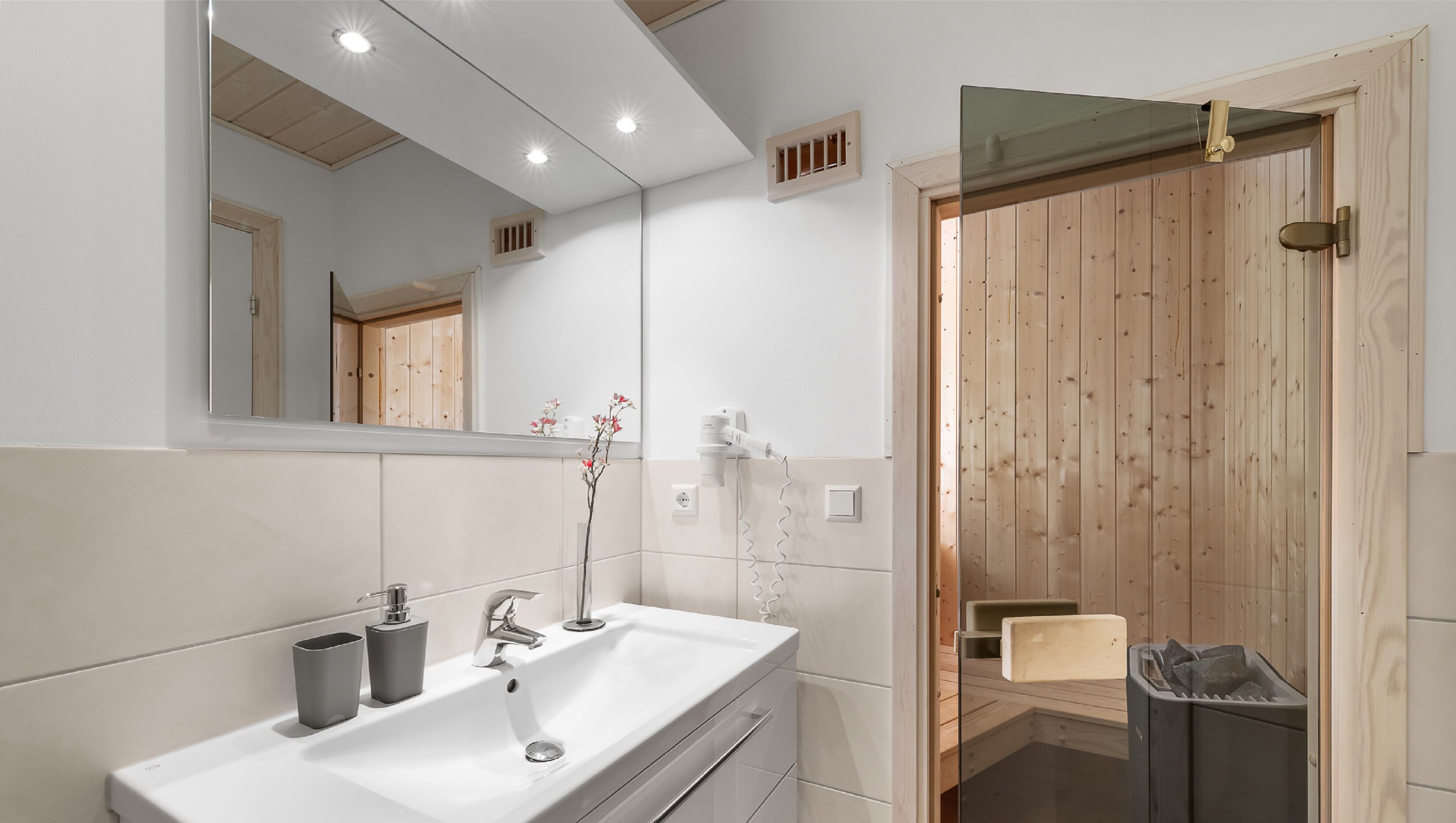 A modern bathroom with a white sink, mirror, and wooden door.