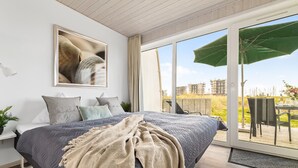 A bedroom with a large bed, a view of the outside, and a window with a curtain. - Ferienhaus Sonnenblume Marina Wendtorf (Wendtorf)