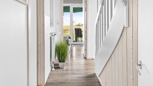 A hallway with wooden flooring, white walls, and a view to an outdoor area with a table and chairs.