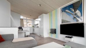 Un salon moderne avec un canapé gris, une table basse blanche et un grand téléviseur fixé au mur.