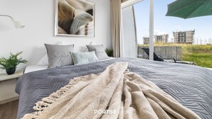 A modern bedroom with a large bed, a framed picture on the wall, and a view of construction outside.