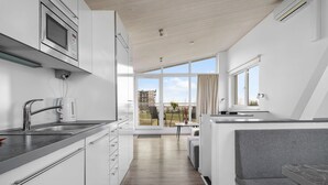 A modern kitchen with a built-in oven, a coffee machine, and a sink. There is a dining area with a table and chairs, and a view of the outside.