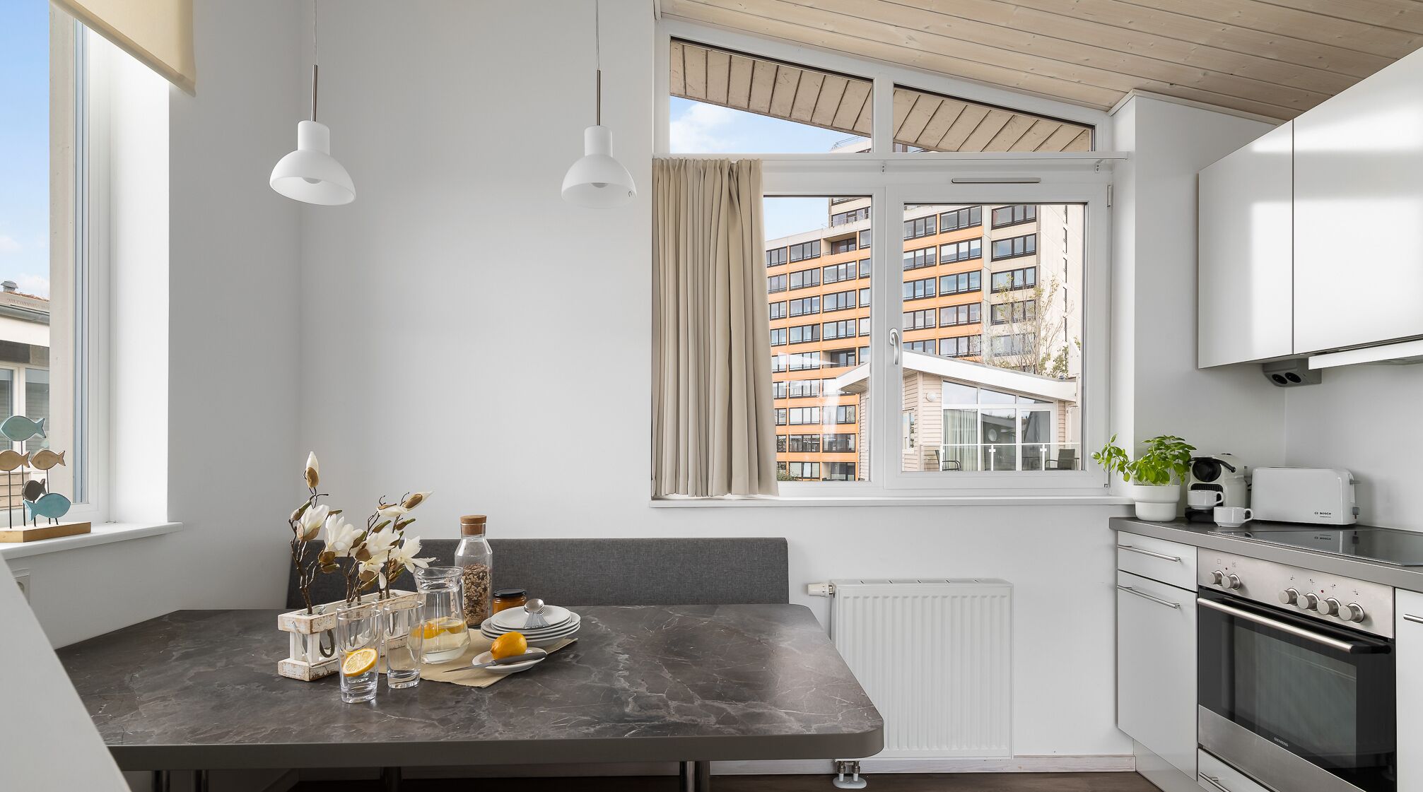 A modern kitchen with a dining area, a built-in oven, and a view of a residential building.