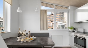 Une cuisine moderne avec un coin repas, un four encastré et une vue sur un immeuble d’habitation.