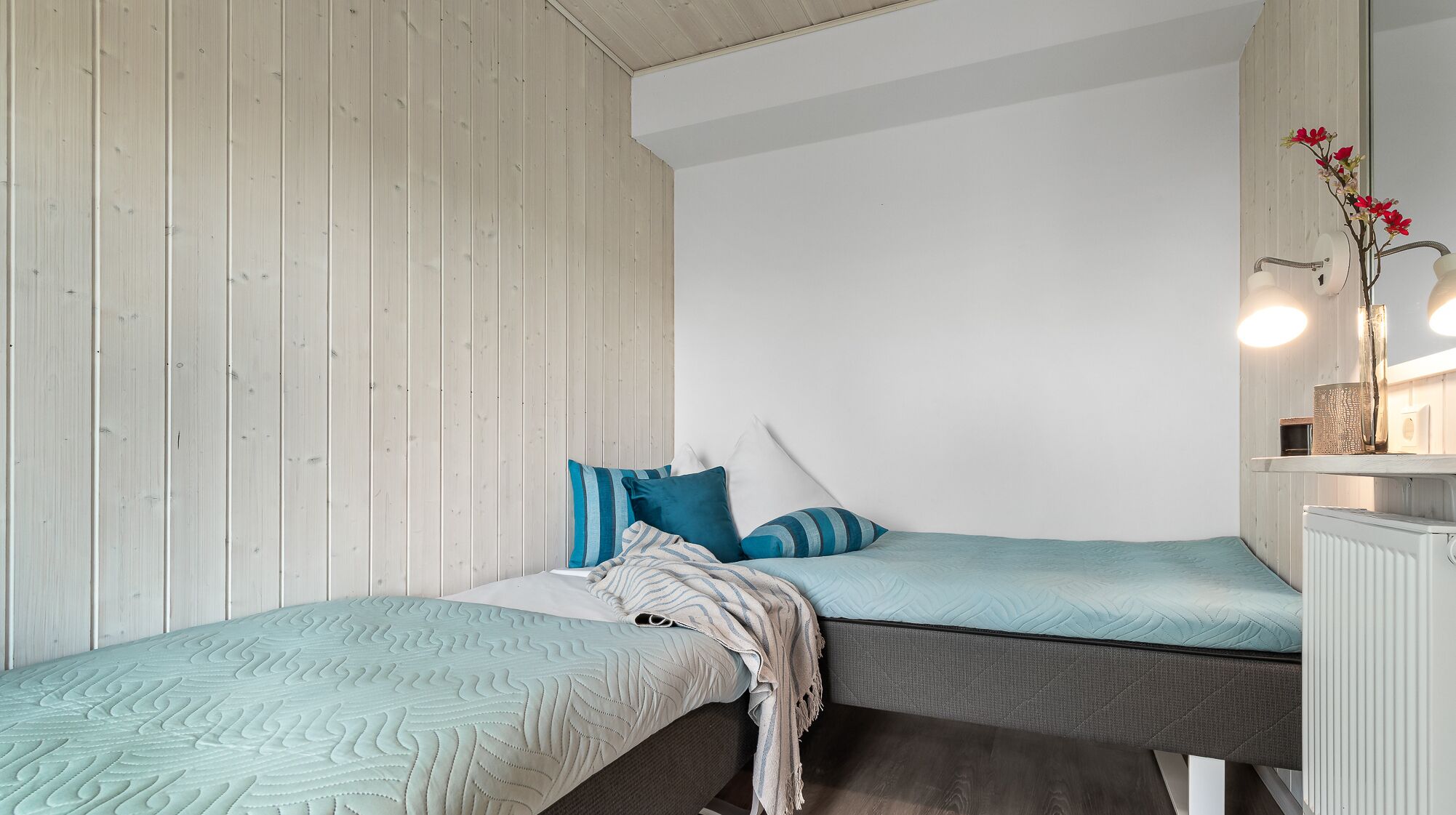 Une chambre avec deux lits, un mur en bois, un plafond blanc et une table de chevet avec une lampe.