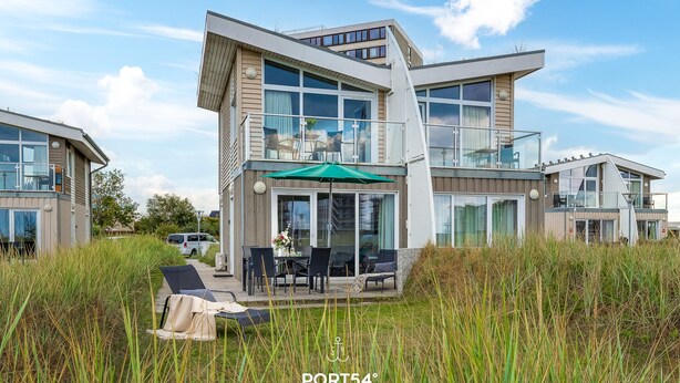 A modern two-story house with a balcony, outdoor seating area, and a green umbrella.