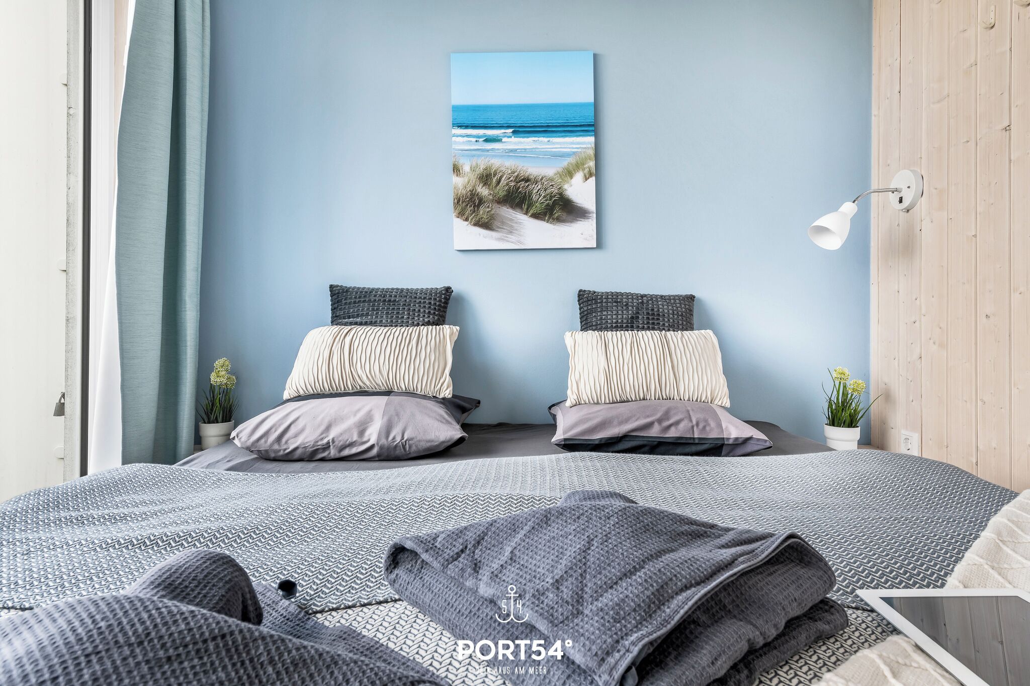 Ein Schlafzimmer mit einem Bett, Kissen, einer Wandlampe und einem Gemälde zum Thema Strand.
