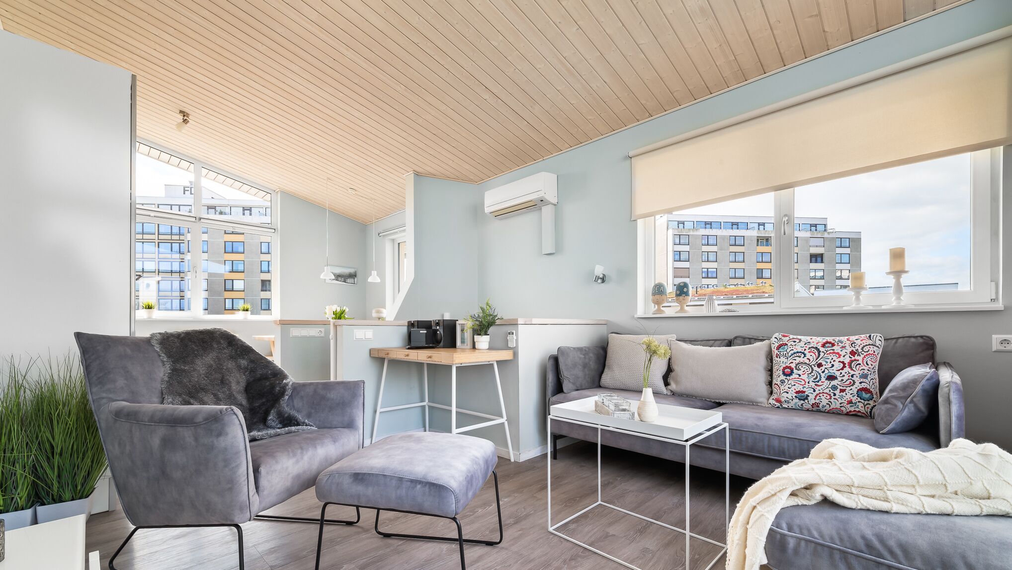 Een moderne woonkamer met een grijze bank, een grijze fauteuil en een salontafel. Er is een raam met uitzicht op gebouwen.