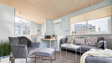 Een moderne woonkamer met een grijze bank, een grijze fauteuil en een salontafel. Er is een raam met uitzicht op gebouwen.