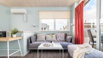 A modern living room with a grey sofa, a white coffee table, and a view of a cityscape through large windows.