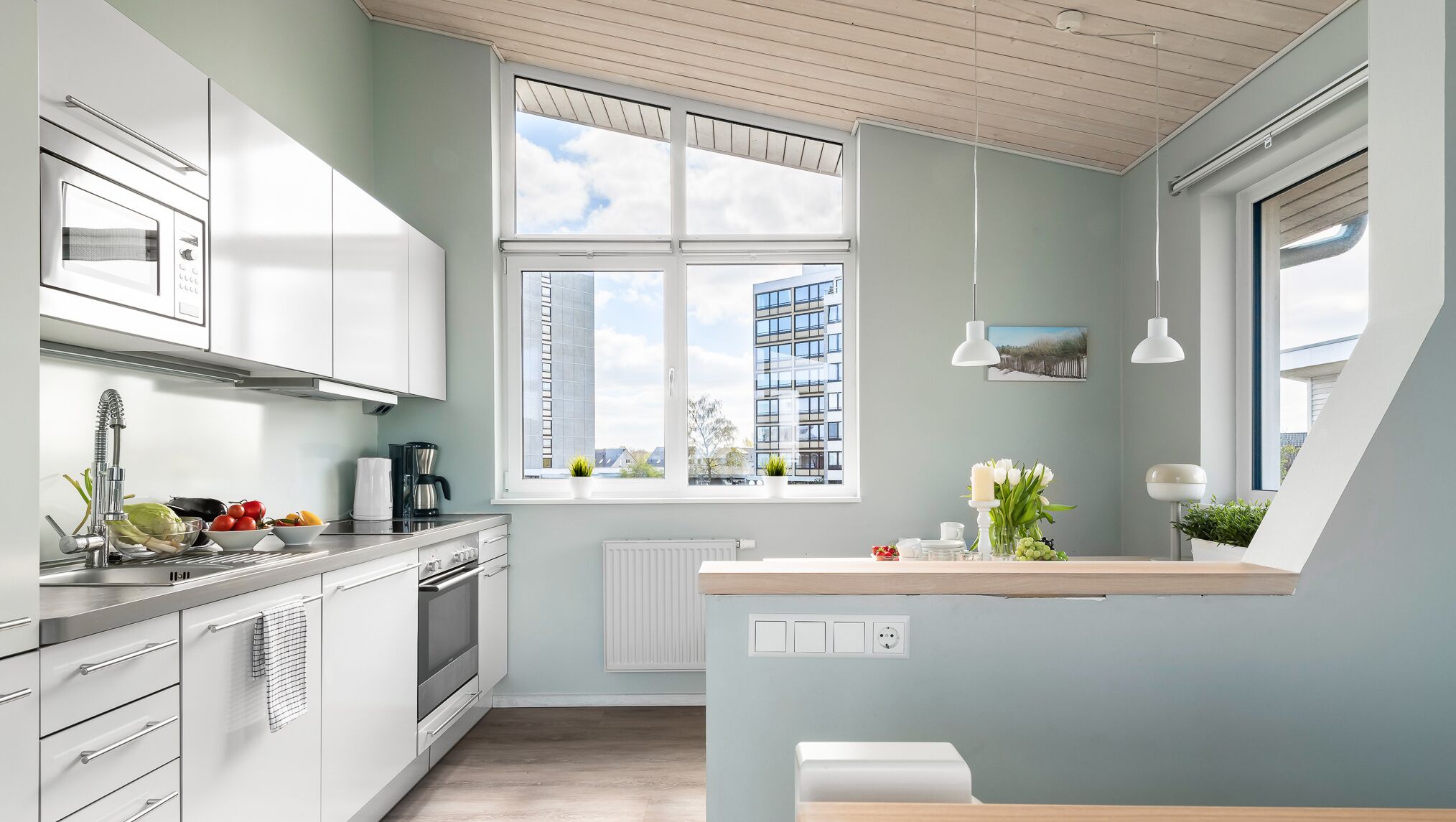 Eine moderne Küche mit weißen Schränken, einem Einbauofen und einem Fenster mit Blick auf die Stadt.
