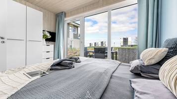 Ein modernes Schlafzimmer mit Bett, Nachttisch und Blick auf Gebäude durch große Fenster.