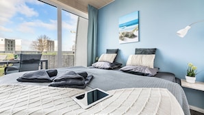 A modern bedroom with a large bed, a tablet on the bed, and a view of the city through large windows.