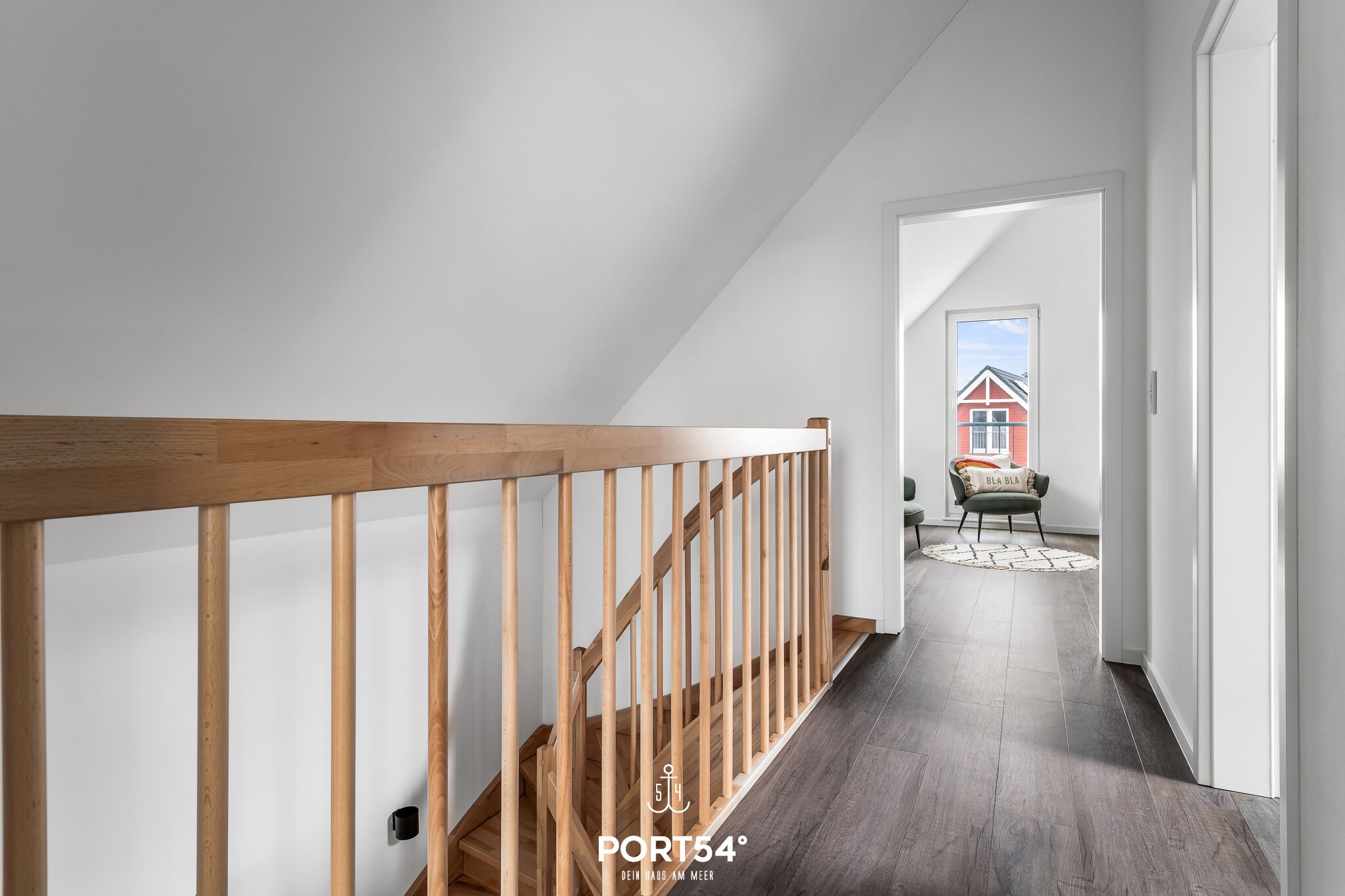 Un intérieur moderne avec un escalier en bois menant à une pièce d’où l’on peut admirer une maison rouge.