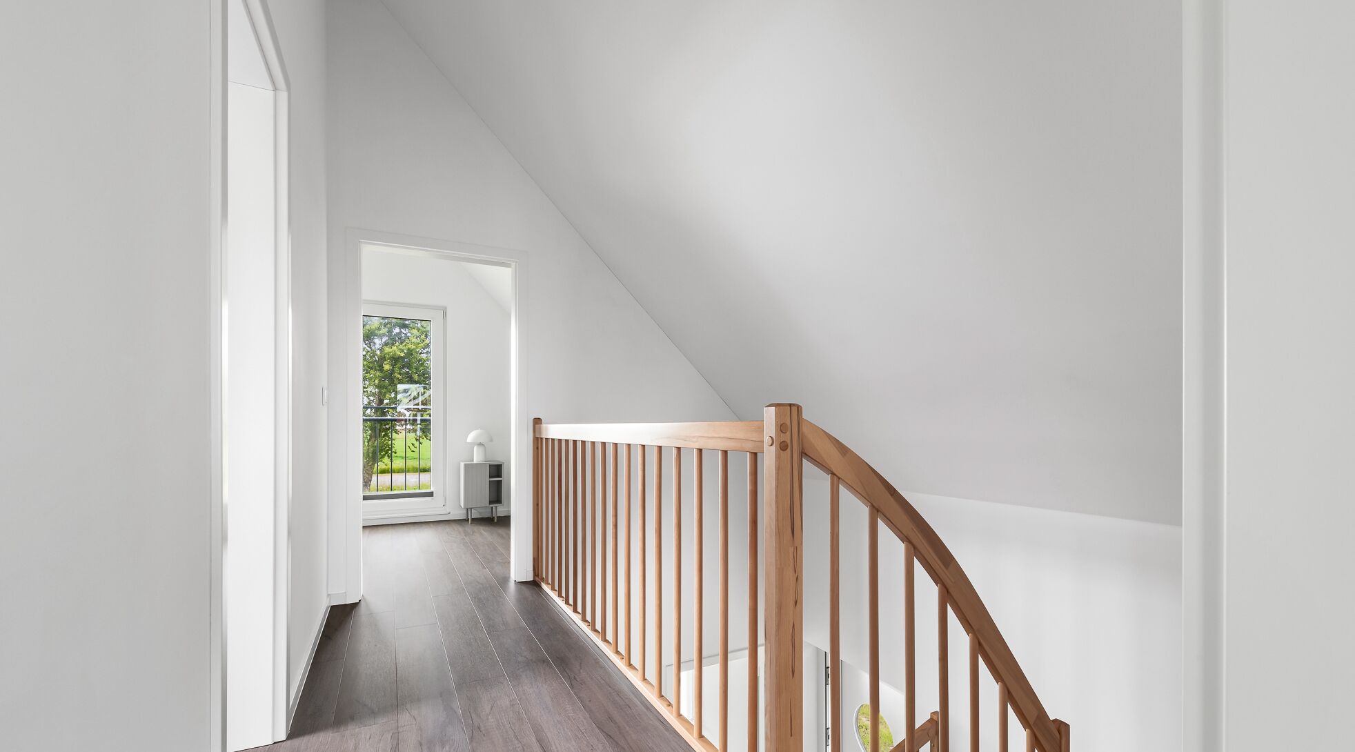 Ein modernes Interieur mit einer Holztreppe, Blick auf einen Balkon und einer Tür zu einem anderen Raum.