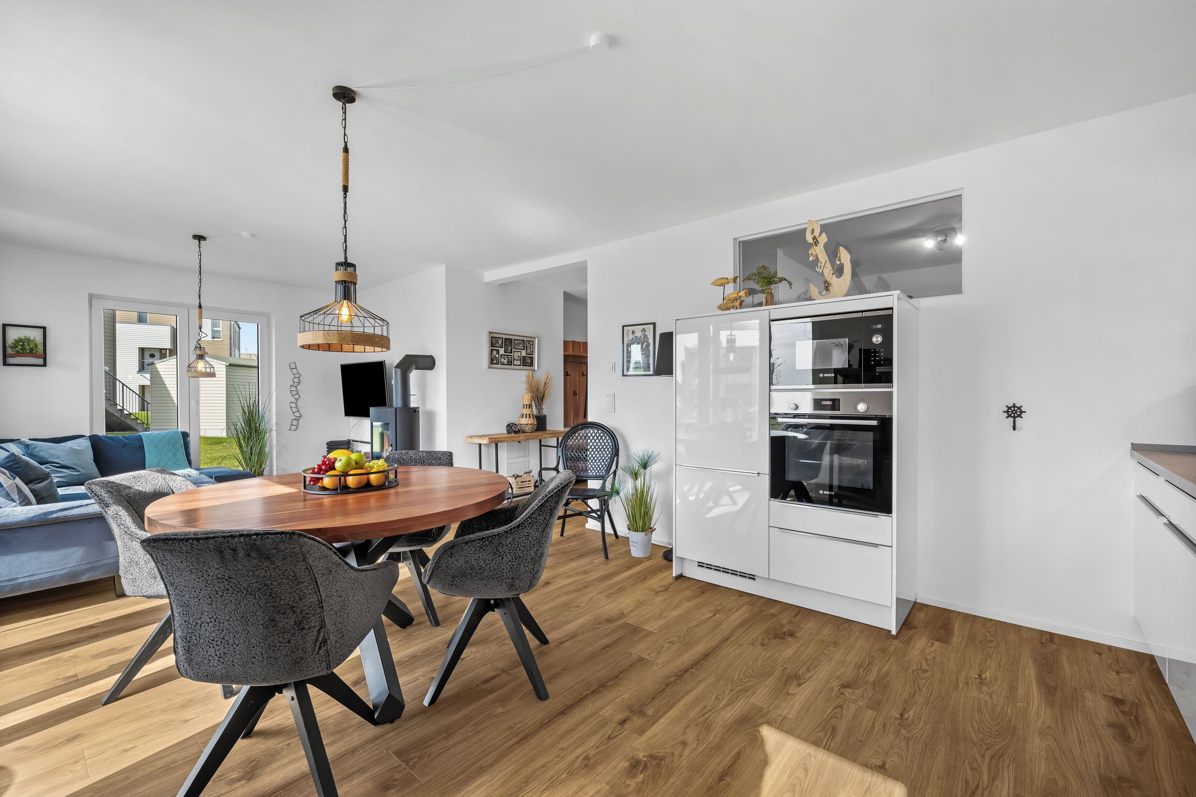 Une cuisine moderne avec des meubles blancs, un réfrigérateur Bosch et un coin repas comprenant une table et des chaises en bois.