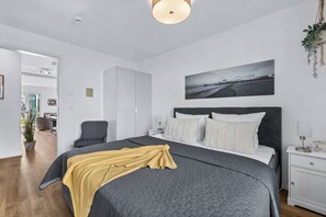 Ein modernes Schlafzimmer mit einem großen Bett, einer Kopfteil, einem Nachttisch, einem Sessel und einer Wandpflanze.