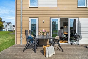 Eine Terrasse mit Tisch, Stühlen, einem Grill und Blick auf die Nachbarschaft.