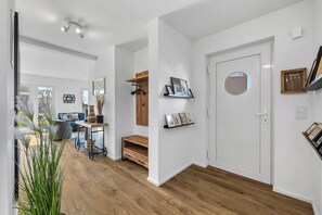 Un intérieur moderne avec un plancher en bois, une porte blanche dotée d’une fenêtre ronde et un porte-manteau sur lequel sont suspendus des vêtements.