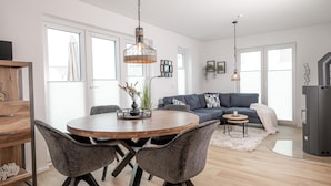 Ein modernes Wohnzimmer mit einem runden Holzes Esstisch, grau gepolsterten Stühlen, einem dunkelblauen Sofa und einem kleinen Beistelltisch.