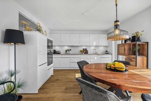 Eine moderne Küche mit weißen Schränken, einem Holzespeisetisch mit Stühlen und einer Pendelleuchte.