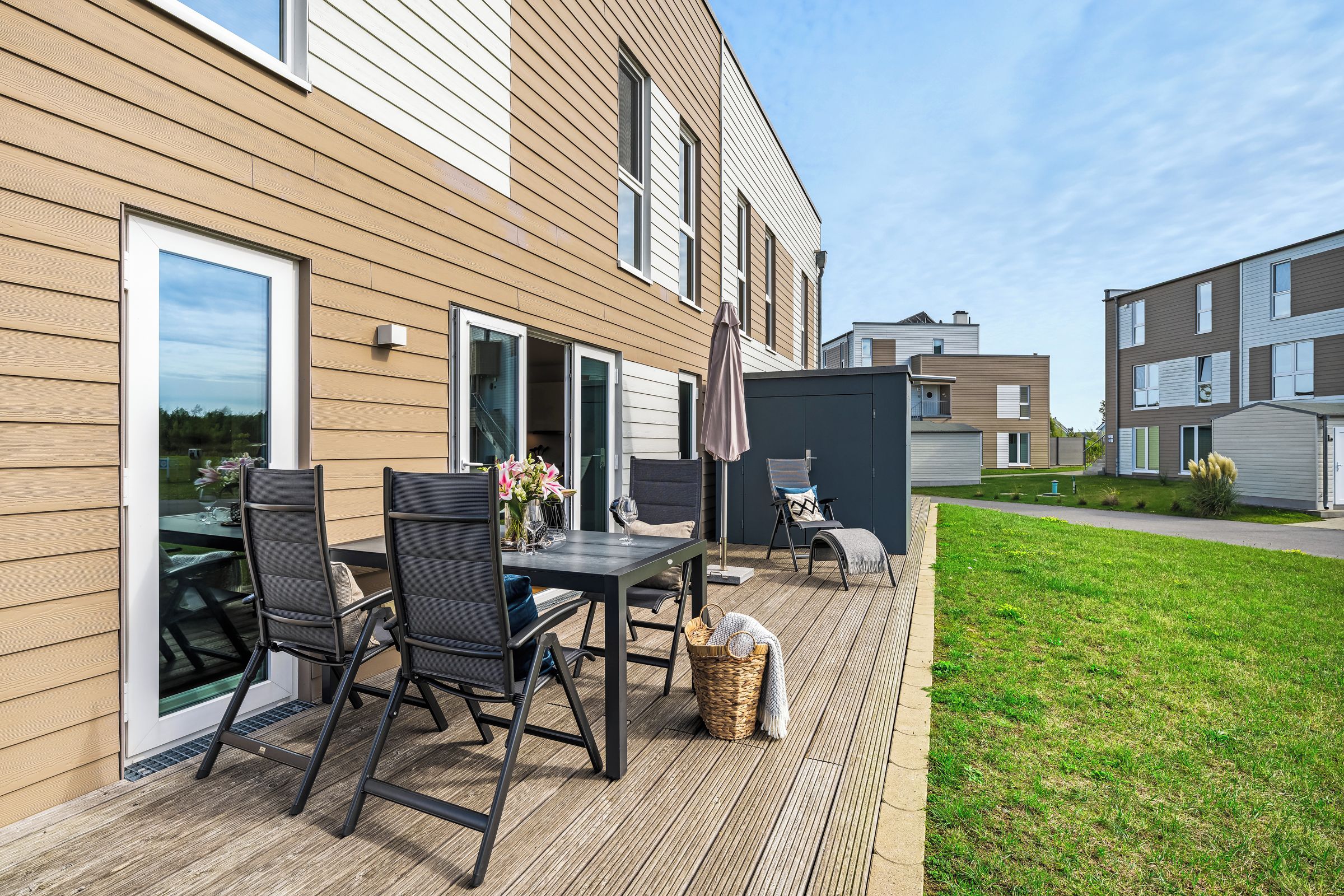 A modern outdoor patio with a table and chairs, a covered seating area, and a view of neighboring buildings.
