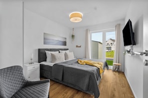 A modern bedroom with a bed, bedside table, chair, and a view of the outside.