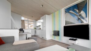 Ein modernes Wohnzimmer mit einem grauen Sofa, einem kleinen weißen Tisch und einem farbenfrohen, abstrakten Wandbild.
