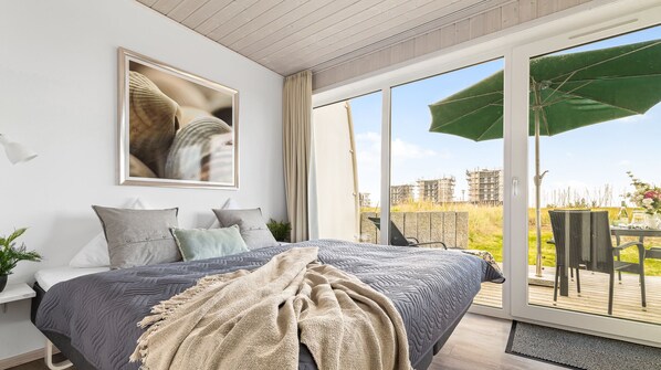Ein modernes Schlafzimmer mit einem großen Bett, einem gerahmten Bild und Blick ins Freie.
