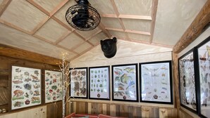 A cozy room with wooden walls, a red sofa with patterned cushions, and framed wildlife and plant illustrations on the walls. - Adorable Cottage in National Forest -- hiking & climbing steps from your door! (Dumont)