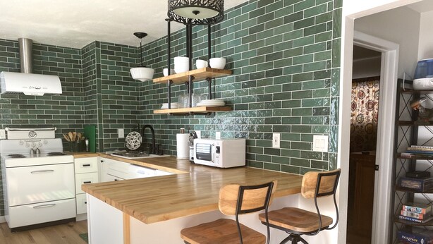 A kitchen with green brick backsplash, white appliances, wooden bar stools, and a built-in island. - Adorable Cottage in National Forest -- hiking & climbing steps from your door! (Dumont)