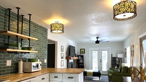 A modern kitchen with white cabinets, a wooden countertop, and a green backsplash. There is a dining area with a green sofa and a wooden table. - Adorable Cottage in National Forest -- hiking & climbing steps from your door! (Dumont)