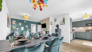Un comedor moderno con una mesa de madera preparada para cuatro comensales, sillas color turquesa y una lámpara de araña colorida.