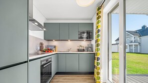 Una cocina moderna con gabinetes grises, horno empotrado y vista a un barrio residencial.