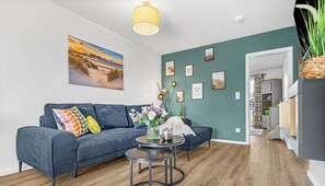 A modern living room with a blue sofa, a round coffee table, and a painting of a sunset.