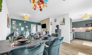 A modern dining area with a wooden table set for four, teal chairs, and a colorful chandelier. - Tüddelbüddel - Infrared Sauna, Bathtub, Fireplace, Terrace, Grill, Parking (Olpenitz)