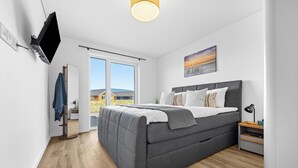 Ett modernt sovrum med en säng, en tv som är monterad på väggen, ett stort fönster och en tavla.