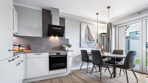 A modern kitchen with white cabinets, a built-in oven, and a dining area with a table and chairs. - Ferienhaus Hannes Büsum (Büsum)
