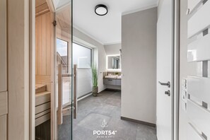 A modern hallway with a glass door leading to a bathroom, a wooden staircase, and a view of the outside. - Ferienhaus Hannes Büsum (Büsum)