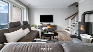 A modern living room with a sofa, a coffee table, a fireplace, and a TV mounted on the wall. - Ferienhaus Hannes Büsum (Büsum)