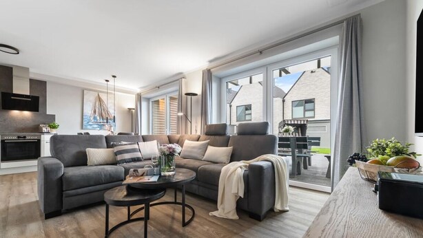 A modern living room with a grey sofa set, a coffee table, and a dining area with a table and chairs. - Ferienhaus Hannes Büsum (Büsum)