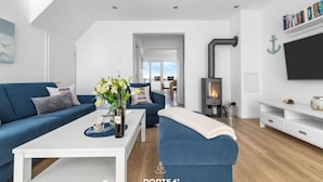 A modern living room with a blue sofa, white coffee table, and a fireplace. - Fjordblick– first row on the water, sauna, whirlpool, shower, fireplace, balcony (Olpenitz)