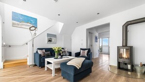 A modern living room with a blue sofa, white coffee table, and a wood-burning stove. - Fjordblick– first row on the water, sauna, whirlpool, shower, fireplace, balcony (Olpenitz)