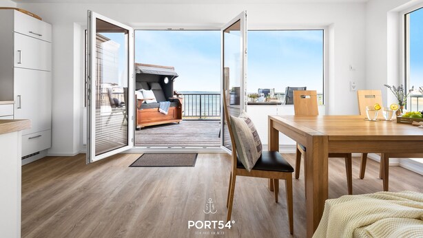 A modern interior with a wooden floor, a dining area with a table and chairs, and a balcony with a sofa and a view of the city. - Fjordblick– first row on the water, sauna, whirlpool, shower, fireplace, balcony (Olpenitz)