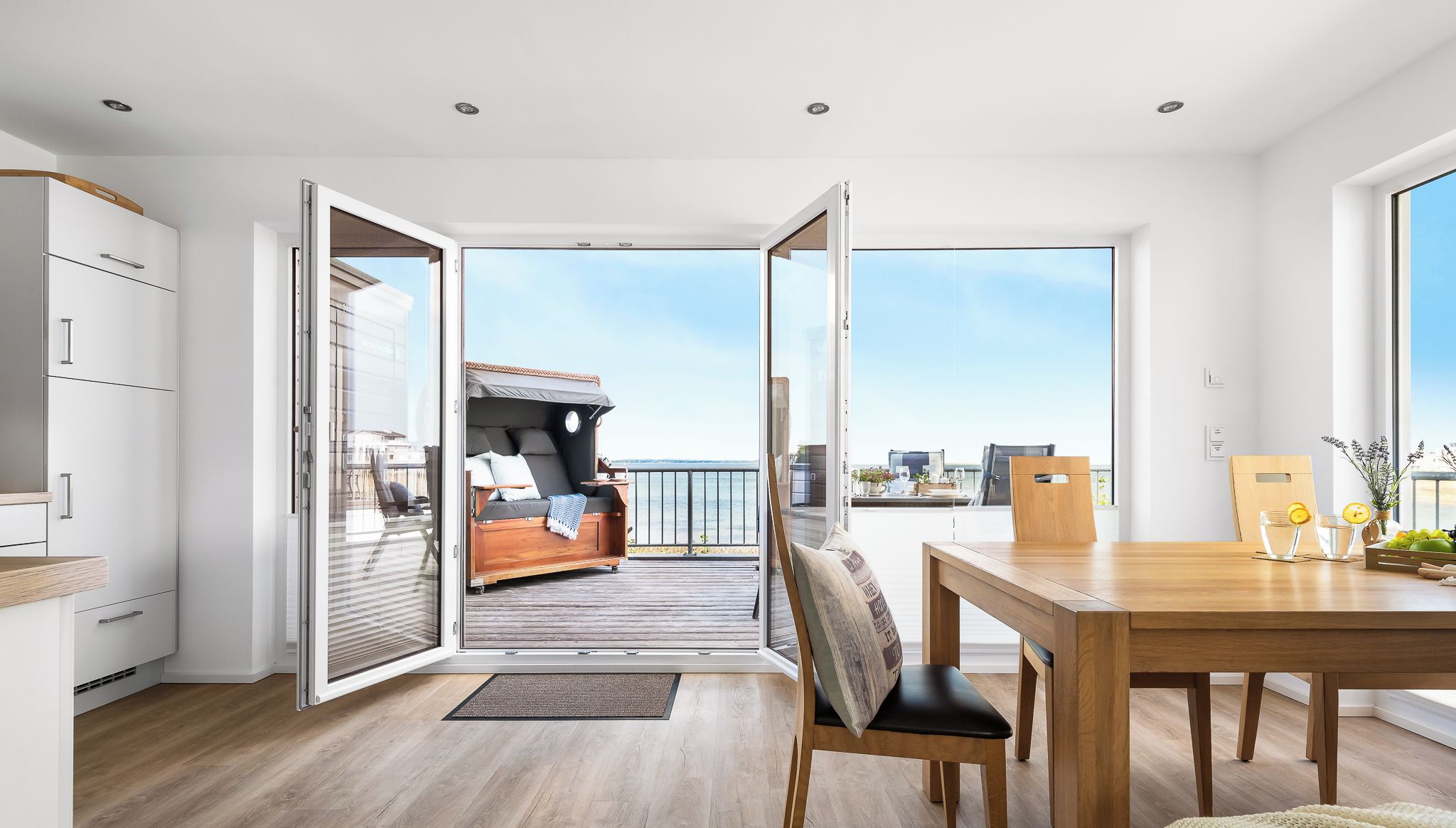 A modern interior with a wooden floor, a dining area with a table and chairs, and a balcony with a sofa and a view of the city.
